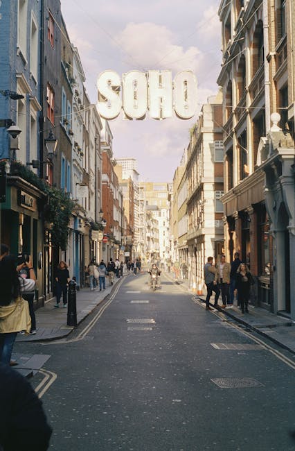 Nighttime scene of Carnaby Street in Soho, with a decorative sign arch reading 'CARNABY' illuminated by multicoloured lights and string lights hanging overhead. On the left, a building with large wind