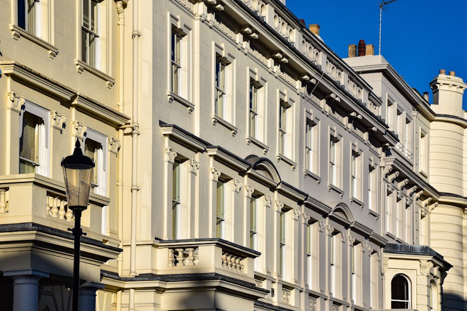 Photograph of a large, historic residential building with ornate cream-colored facades, decorative window frames, and detailed architectural moldings. The building features multiple floors with tall, 